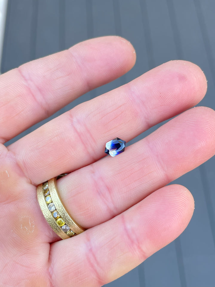 1.10-carat bi-color sapphire in royal blue and faint yellow hues displayed on a hand with a gold ring.