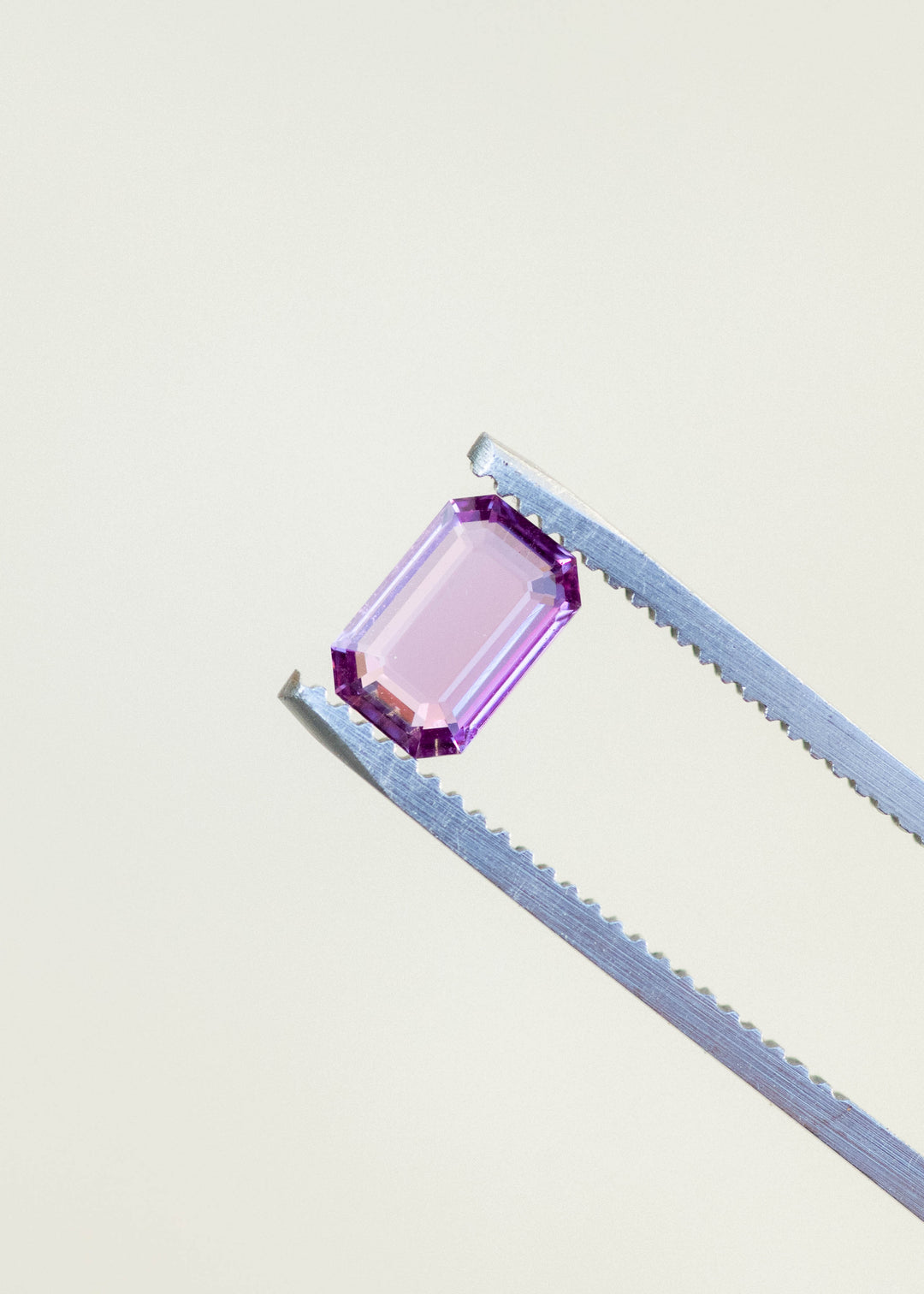 Natural pink sapphire held in tweezers against a white background.