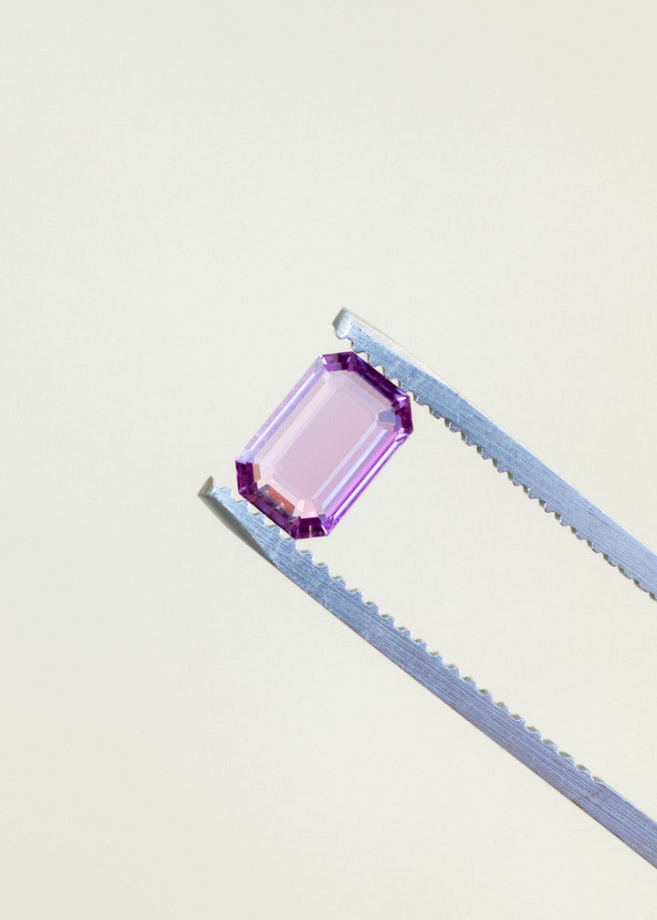 Natural pink sapphire held in tweezers against a white background.
