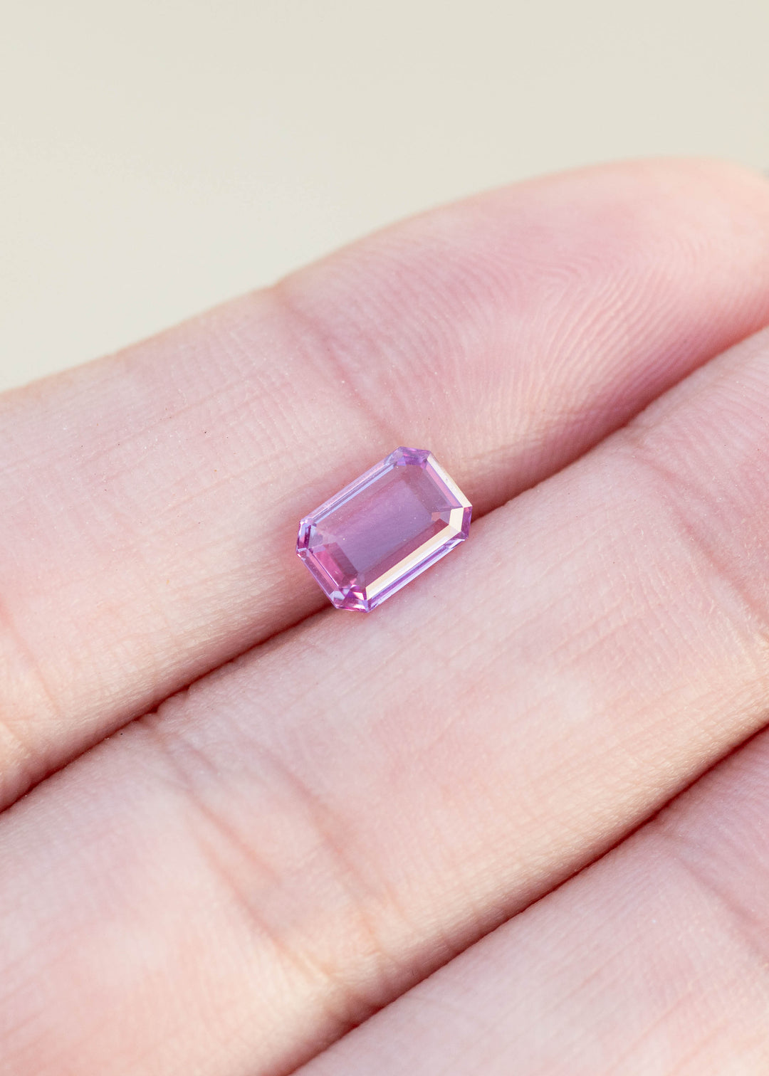 Pink portrait cut sapphire held between fingers against a neutral background
