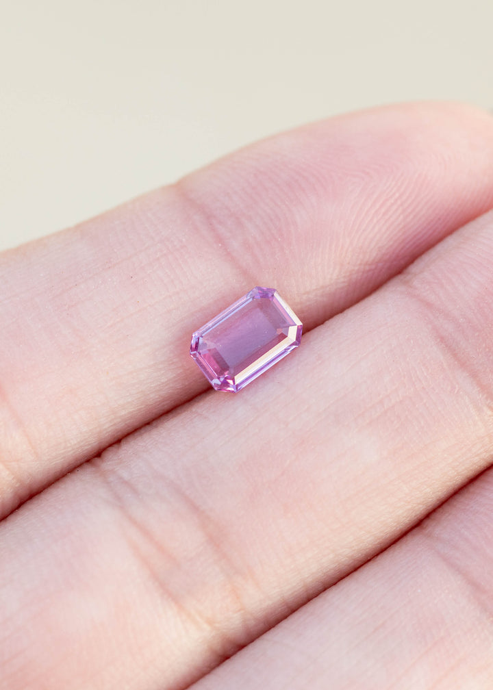 Pink portrait cut sapphire held between fingers against a neutral background