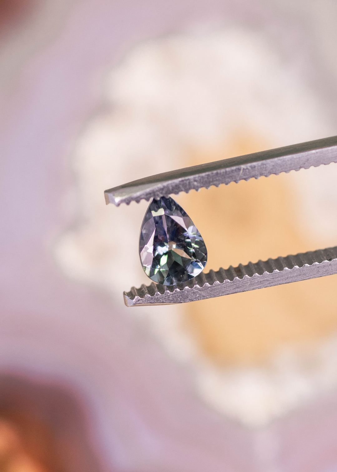 1.10 carat violet teal modified brilliant pear Tanzanite held in tweezers, loose gemstone from Arusha Tanzania displaying strong internal reflections and sharp faceting for bespoke fine jewelry