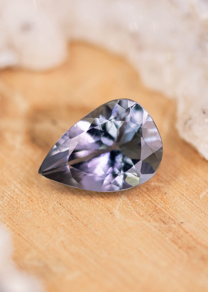 1.10 carat violet teal pear cut Tanzanite displayed on natural stone surface, precision modified brilliant faceted gemstone from Tanzania showing bright brilliance and custom jewelry appeal