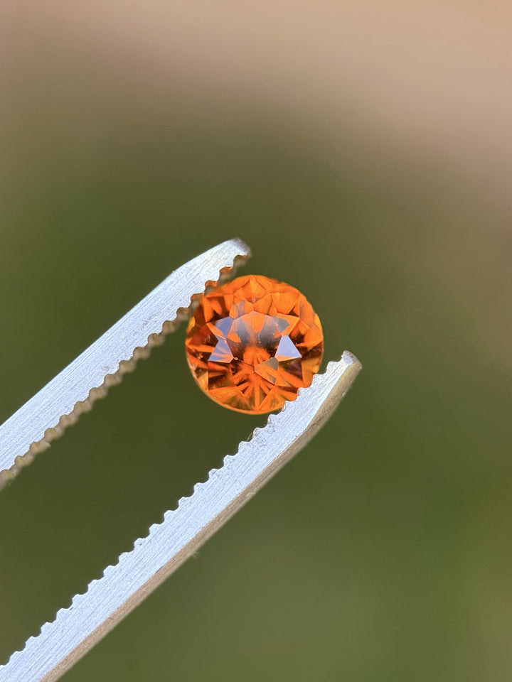 Close-up of Hessonite garnet on a textured gray surface showcasing rich orange-brown fire
