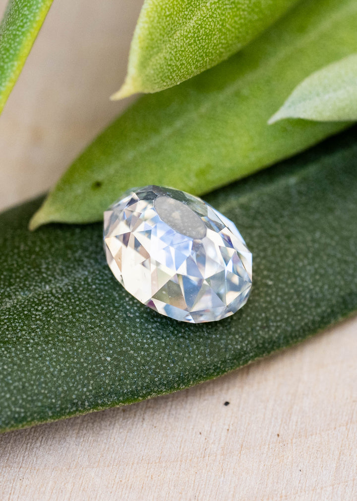 Oval Mughal cut diamond resting on a dark green leaf, photographed at an angle to reveal its dimensional profile and mosaic-like faceting.