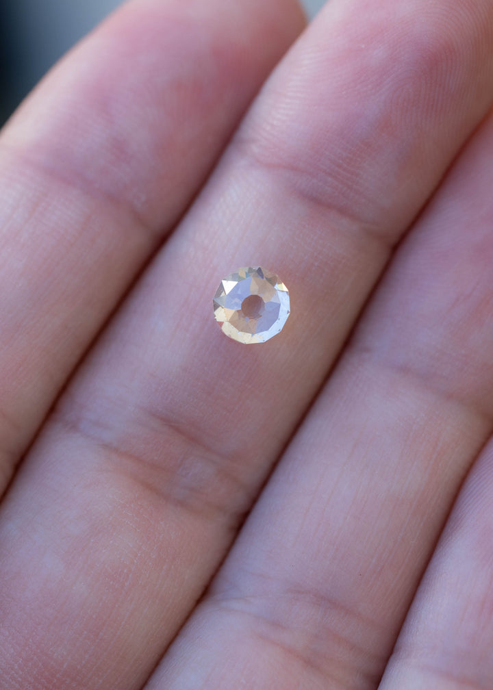 1.11 carat round Mughal cut South African diamond resting on a fingertip for scale, showing its approximately 5.5 mm face-up size and warm appearance.