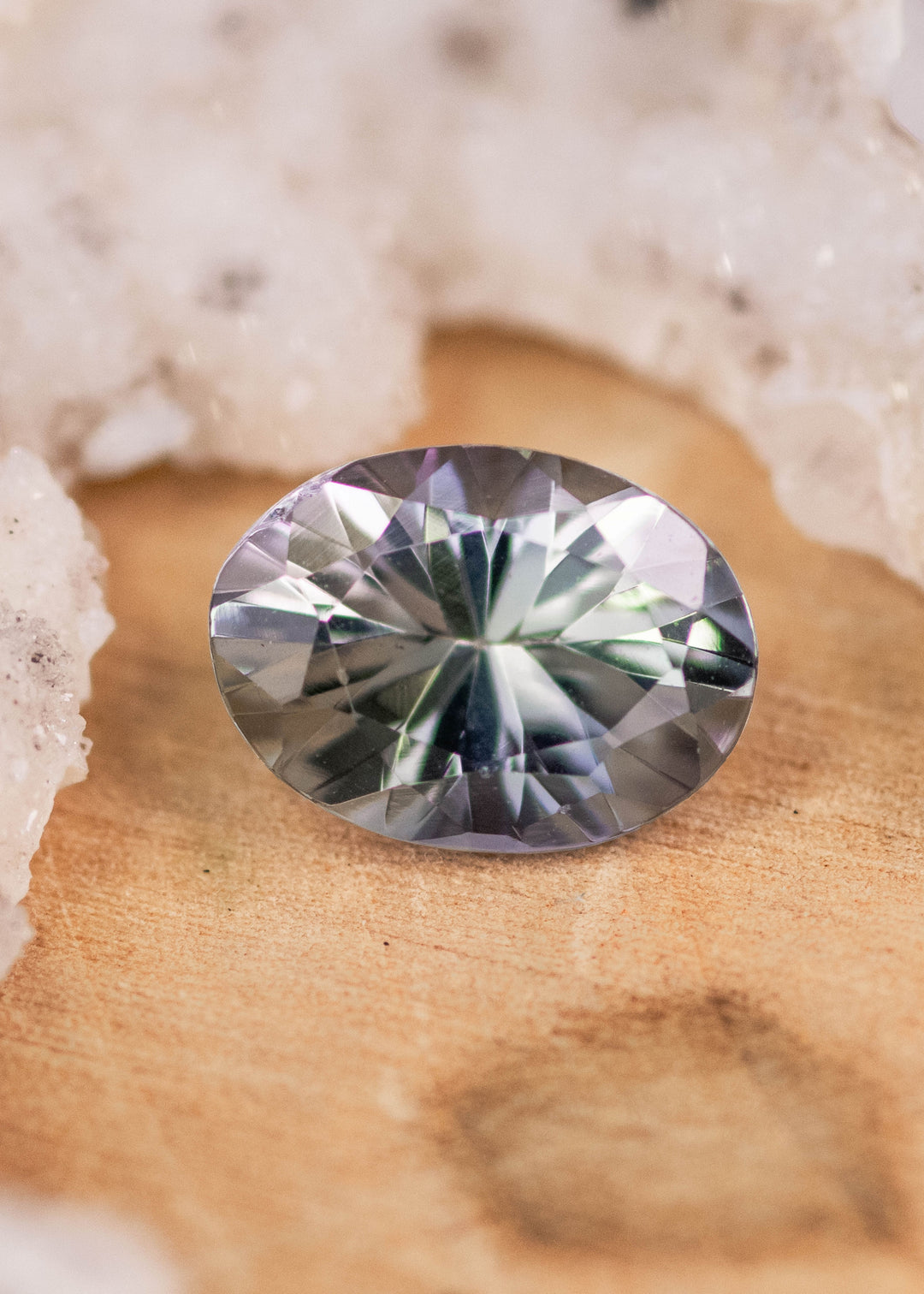 1.11 carat violet teal green oval Tanzanite displayed on natural stone surface, mix modified brilliant faceted gemstone from Arusha Tanzania with crisp symmetry and vibrant light performance