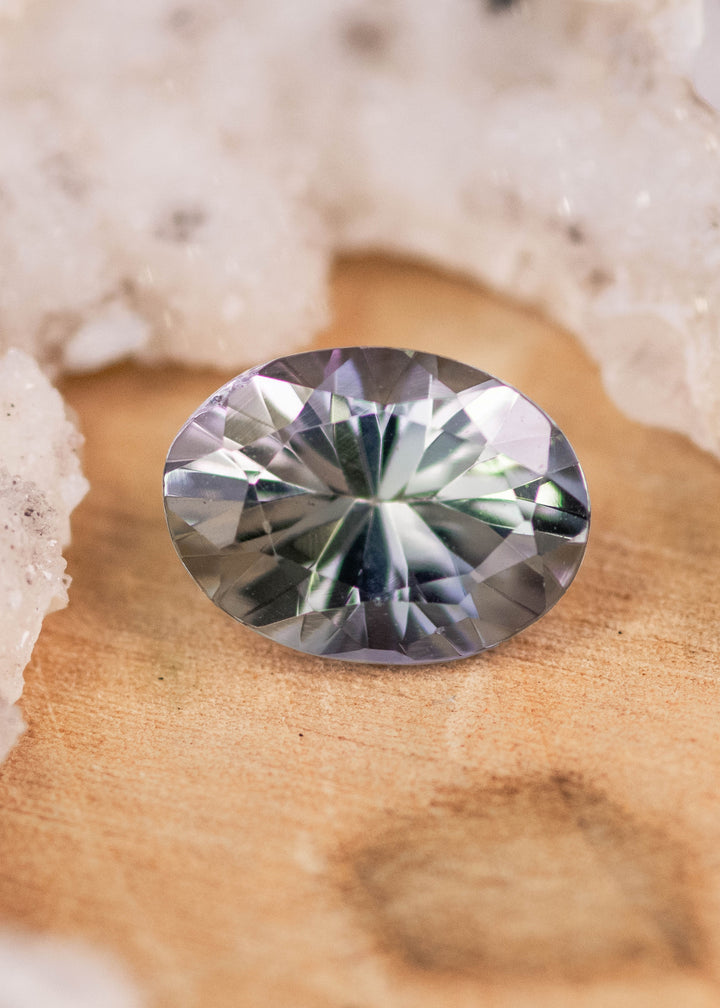 1.11 carat violet teal green oval Tanzanite displayed on natural stone surface, mix modified brilliant faceted gemstone from Arusha Tanzania with crisp symmetry and vibrant light performance
