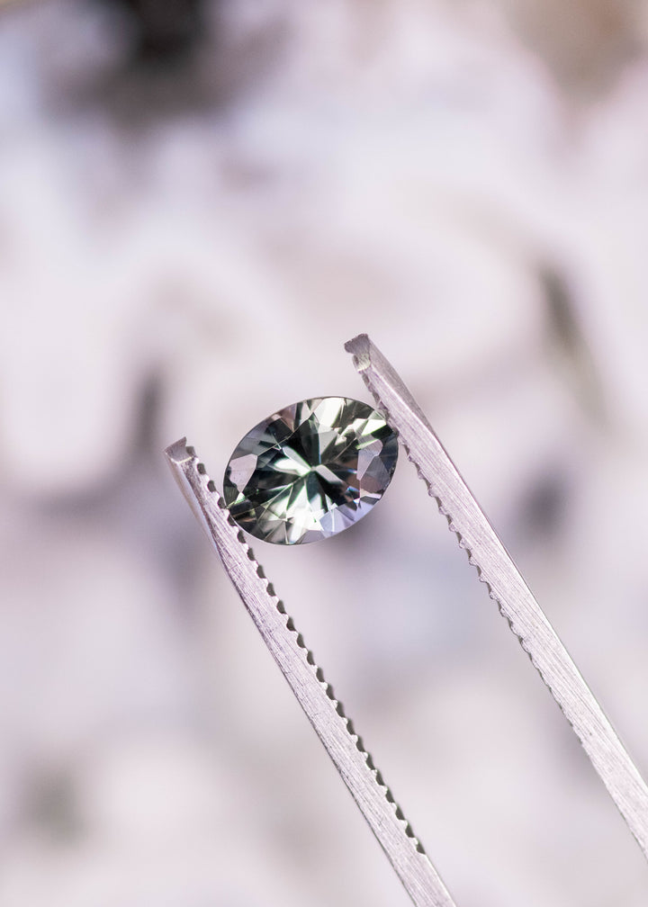 1.11 carat violet teal green oval Tanzanite held in tweezers, precision mix modified brilliant cut gemstone displaying bright internal reflections and strong brilliance for bespoke fine jewelry