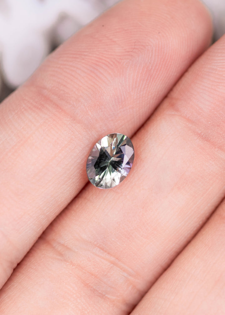 1.11 carat violet teal green oval Tanzanite resting on finger, mix modified brilliant cut from Merelani Hills Tanzania showing starburst faceting and vivid color shift for custom jewelry design
