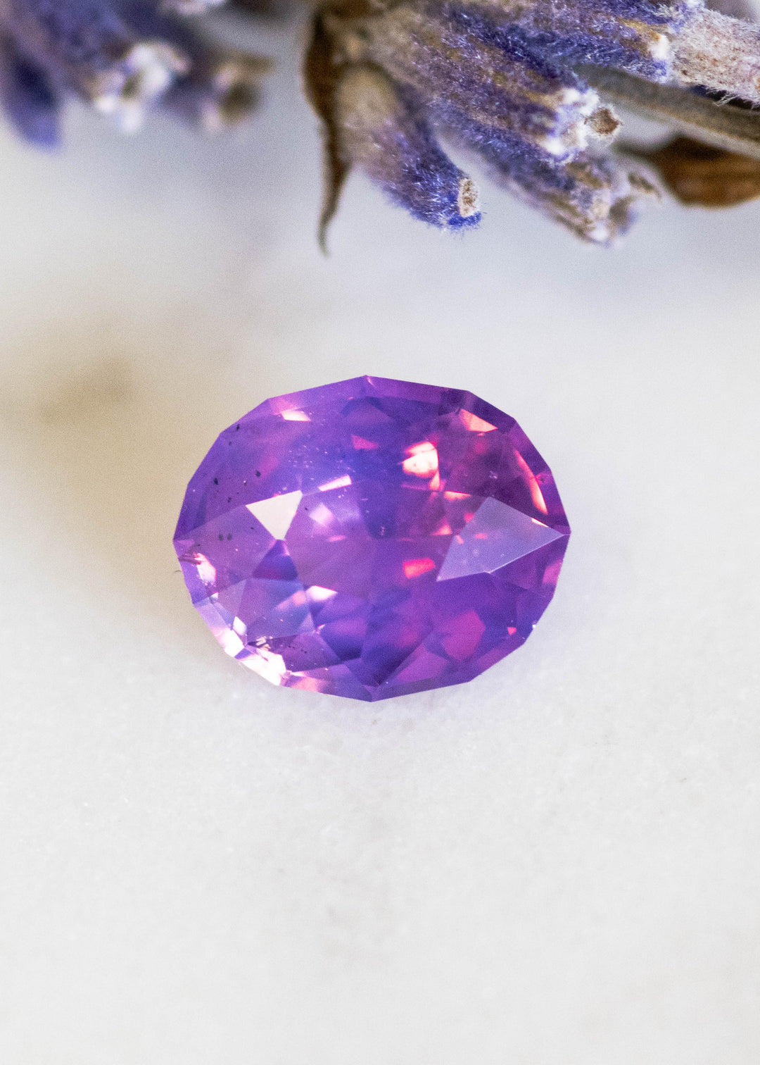 Loose 1.12 carat opalescent purple pink sapphire from Ratnapura shown face-up, displaying the precision oval mix cut and soft pastel glow across the crown facets.