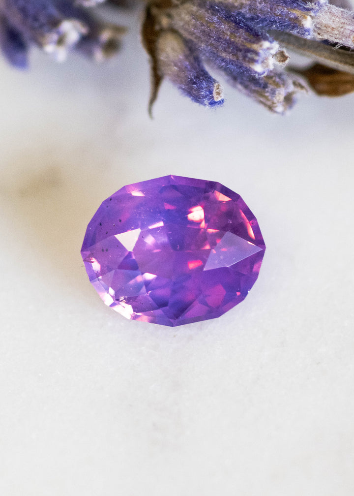 Loose 1.12 carat opalescent purple pink sapphire from Ratnapura shown face-up, displaying the precision oval mix cut and soft pastel glow across the crown facets.