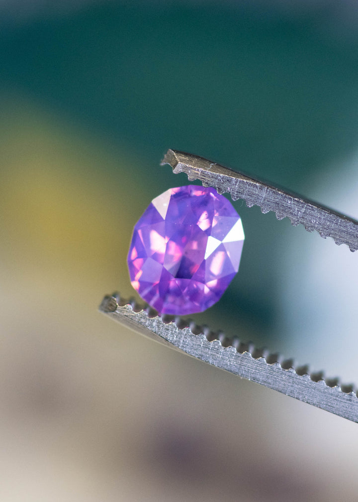 Loose unheated opalescent purple pink sapphire held in tweezers, highlighting crisp facet symmetry and gentle lavender-to-rose color zoning.