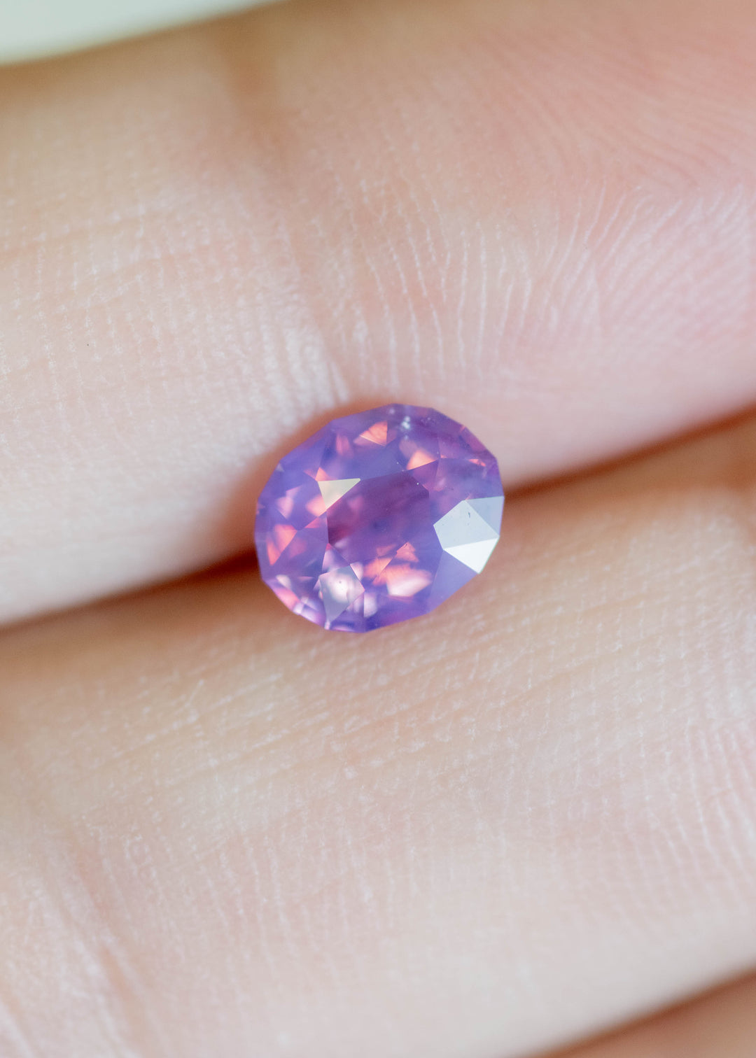 Loose 1.12 carat purple pink sapphire resting on fingertips, revealing balanced oval proportions and subtle opalescent sheen in natural light.