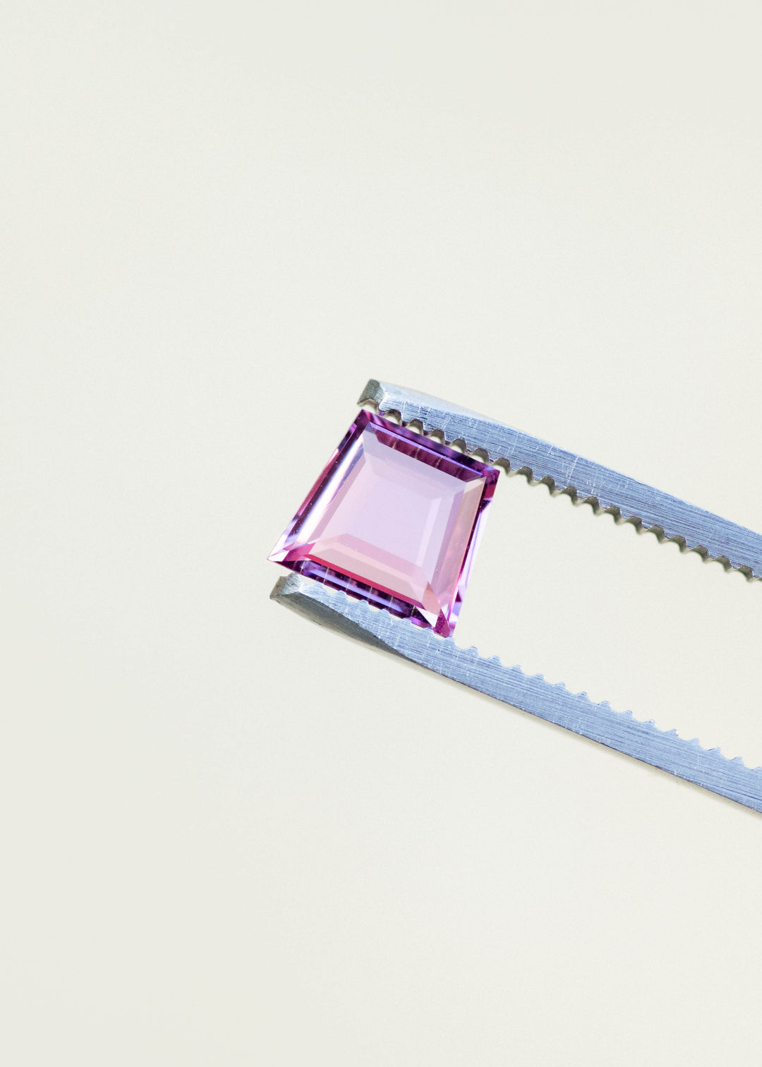 Hot pink natural sapphire in a trapezoid portrait cut held in gem tweezers under natural light.