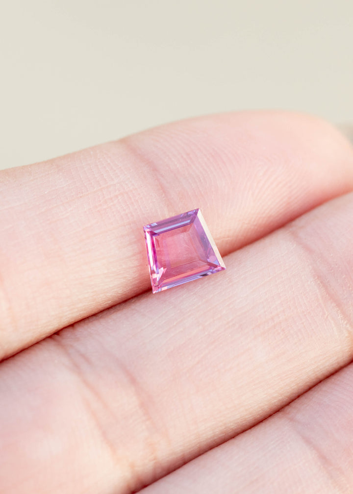 Trapezoidal portrait cut sapphire in natural hot pink color resting on finger tips under natural light.