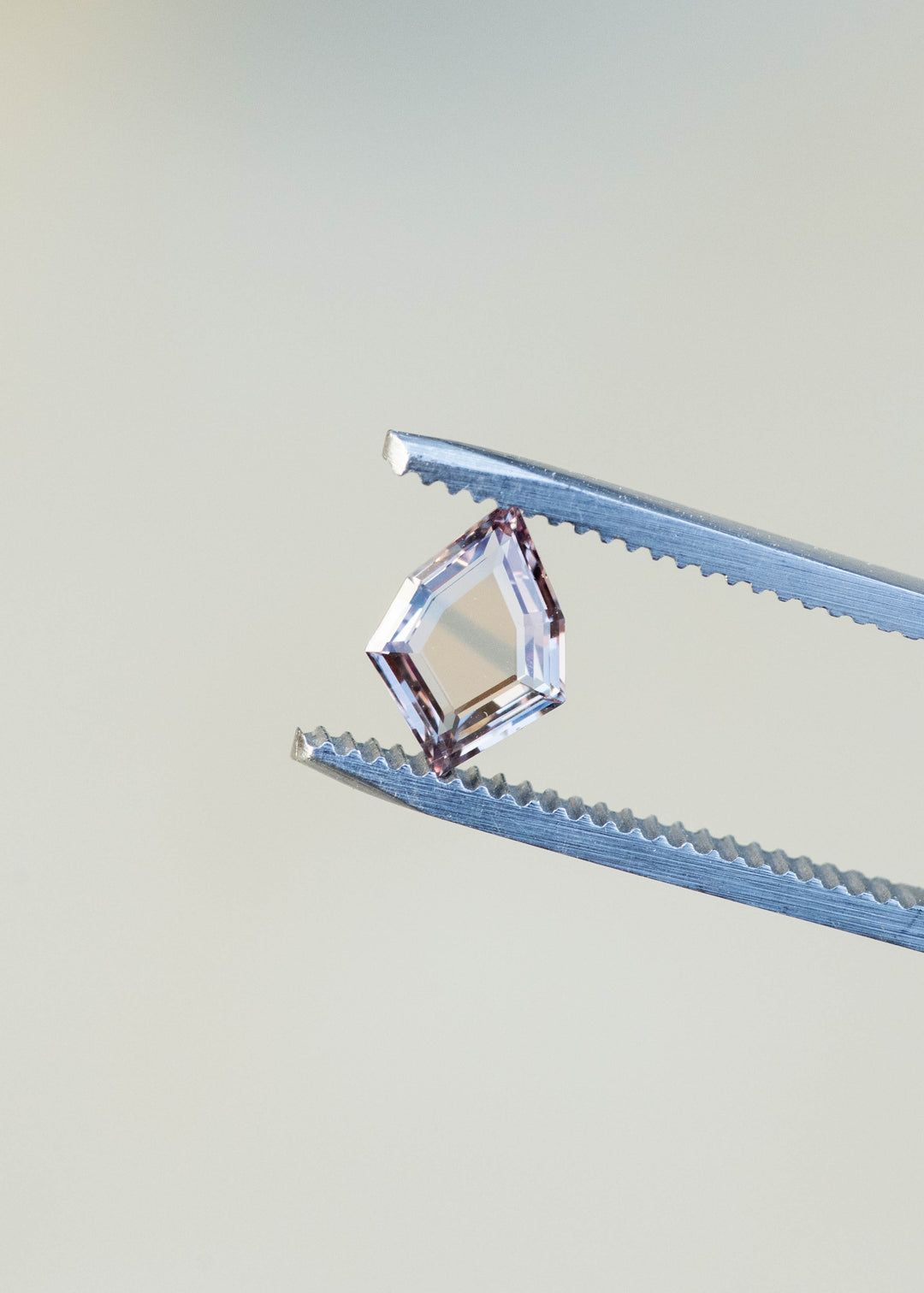 1.12ct peach and blue parti portrait cut sapphire held in gem tweezers in natural lighting.