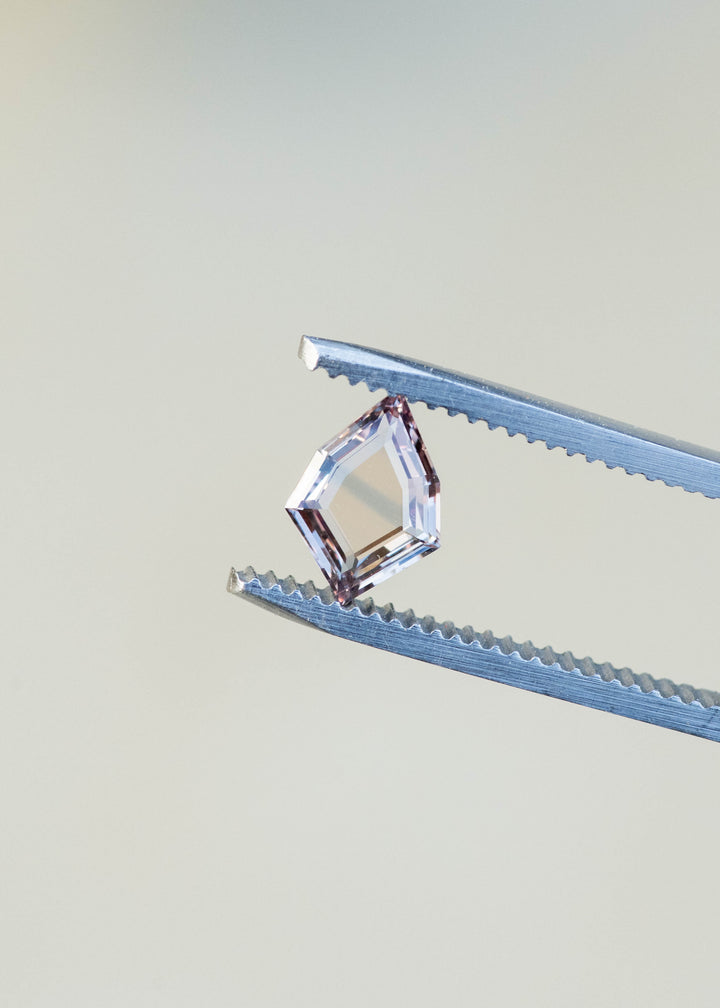 1.12ct peach and blue parti portrait cut sapphire held in gem tweezers in natural lighting.