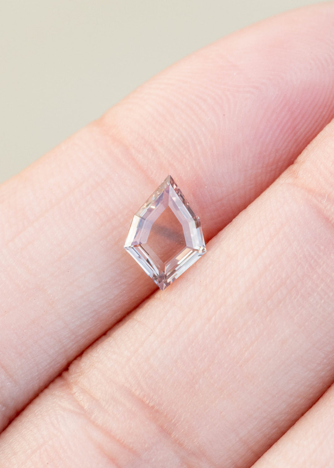 1.12ct peach and blue parti portrait cut sapphire held in fingertips.