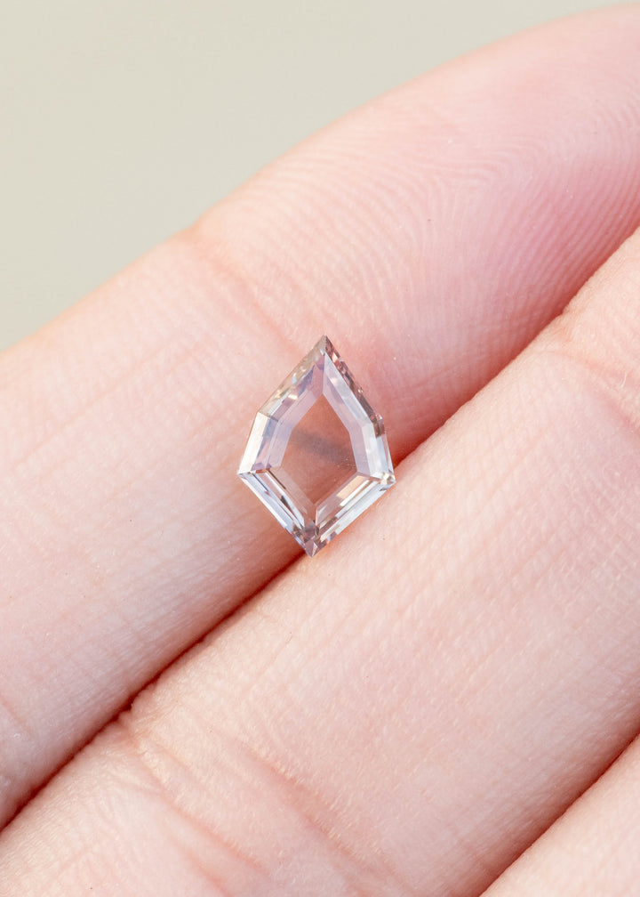 1.12ct peach and blue parti portrait cut sapphire held in fingertips.