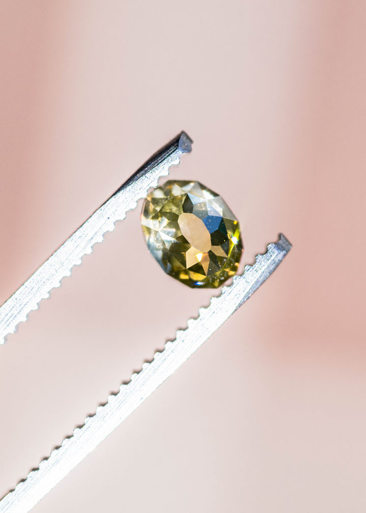 Green gemstone held between tweezers against a pink background