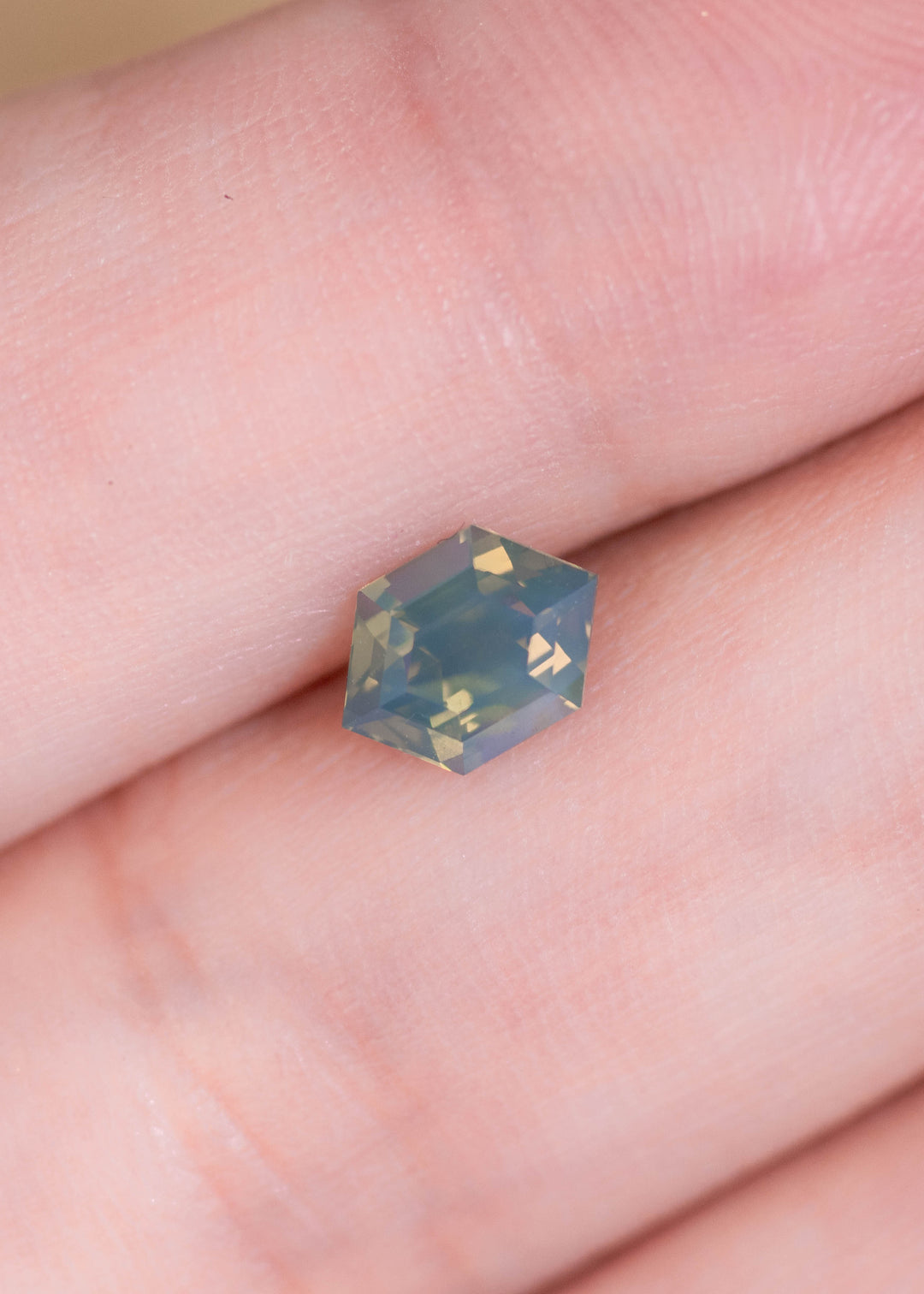 Loose opalescent green yellow sapphire from Sakaraha Madagascar shown on a fingertip highlighting the hexagonal step cut and subtle color shift in natural light.