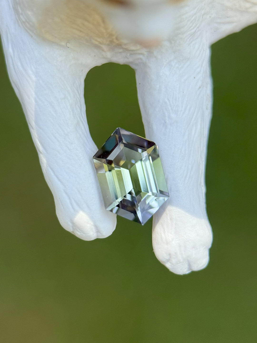 1.14 carat mermaid Tanzanite resting on white cat figurine, showing off its step-cut hexagon shape and vibrant teal, green, and purple hues