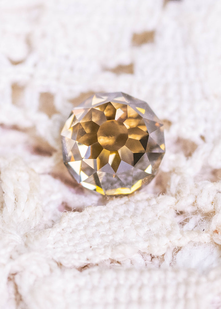 Loose fancy yellow brown Mughal cut diamond resting on textured fabric, highlighting its faceted dome structure and natural golden-brown color.