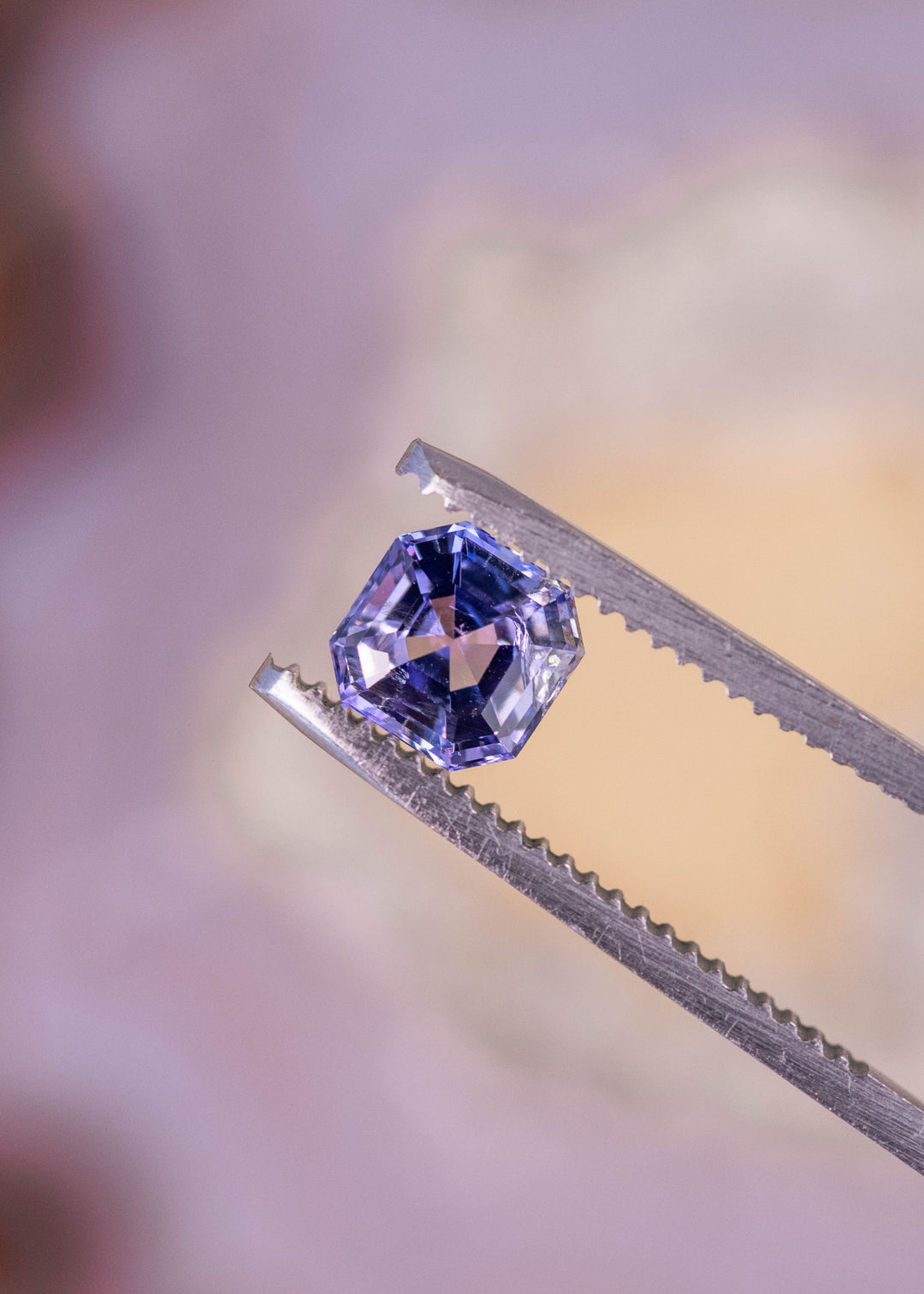 1.14 carat pink purple blue Tanzanite Asscher cut held in tweezers, untreated Merelani Hills Arusha Tanzania gemstone displaying concentric step facets, sharp reflections and vibrant color shift for fine jewelry design