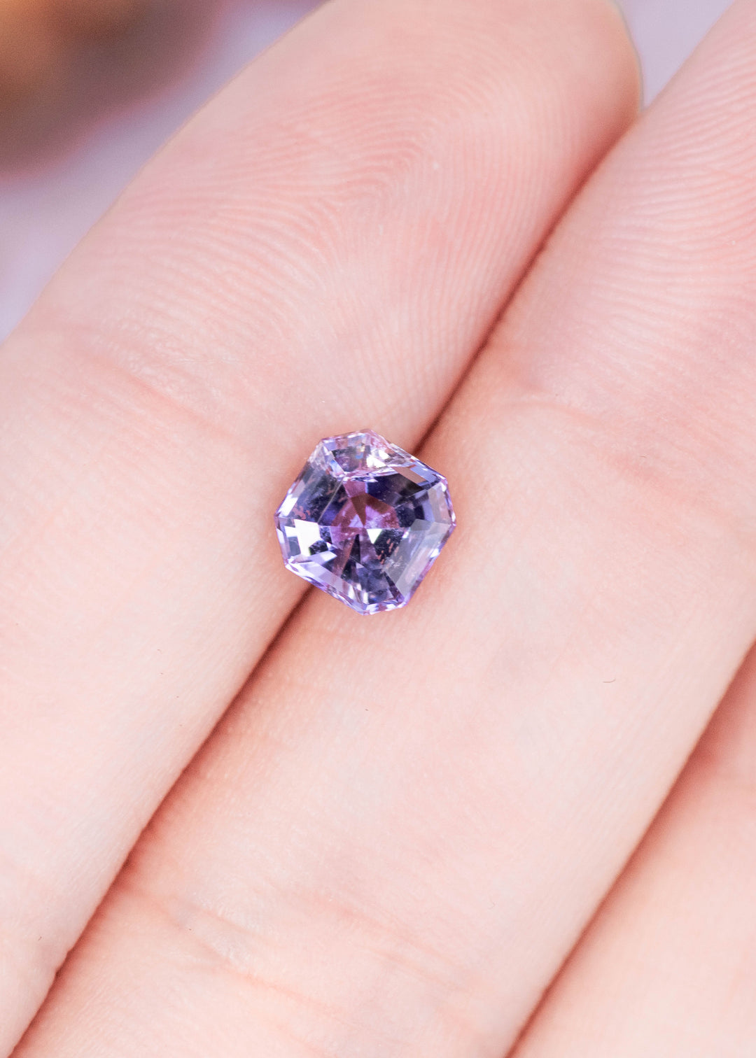 1.14 carat pink purple blue Tanzanite Asscher cut resting on finger, untreated gemstone from Merelani Hills Tanzania showing crisp step cut faceting, geometric symmetry and vivid trichroic color for custom jewelry