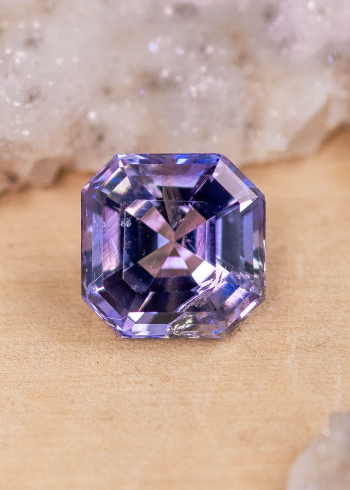1.14 carat pink purple blue Tanzanite Asscher cut displayed on natural surface, precision square step cut gemstone from Tanzania highlighting clarity, symmetry and designer appeal for bespoke jewelry