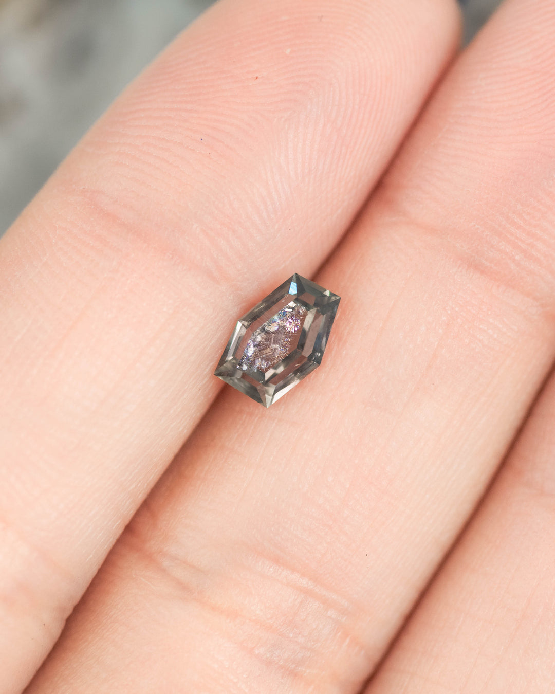 1.15 carat purple pink gray Montana sapphire displayed on fingertip for size reference, custom hexagon portrait cut untreated gemstone from El Dorado Bar Deposit.