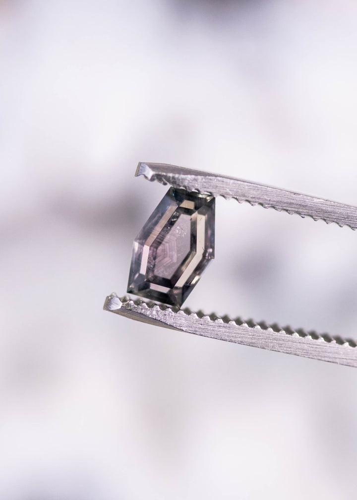 1.15ct untreated Montana sapphire held in gem tweezers, showing custom geometric hexagon portrait cut with purple, pink, and gray color shift from El Dorado Bar Deposit, USA.