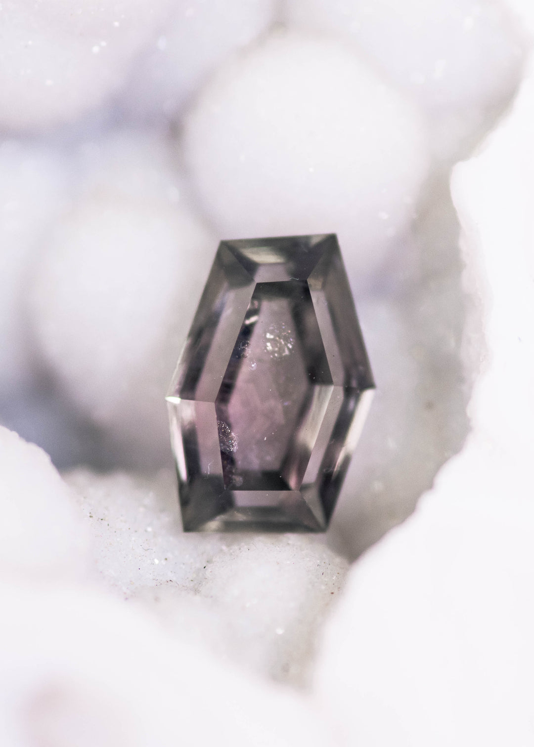 1.15 carat Montana sapphire in purple, pink, and gray tones resting on white crystal matrix, custom geometric hexagon cut from El Dorado Bar Deposit, untreated gemstone photographed in natural light.