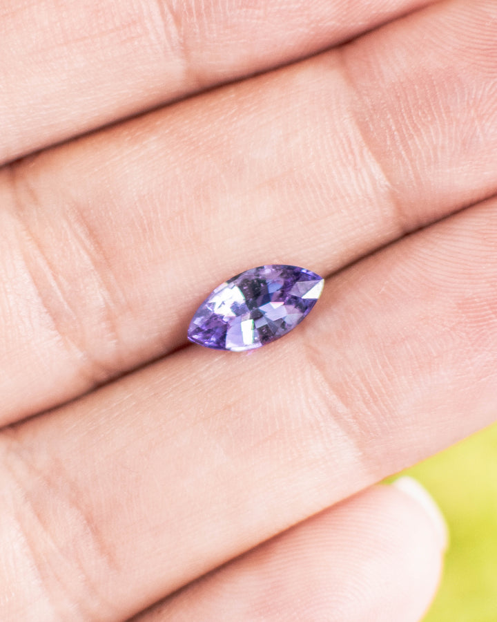 1.15 carat lavender and purple sapphire balanced on a fingertip, revealing its marquise shape and sparkling mixed cut reflections, ethically sourced untreated sapphire from Sakaraha, Madagascar.