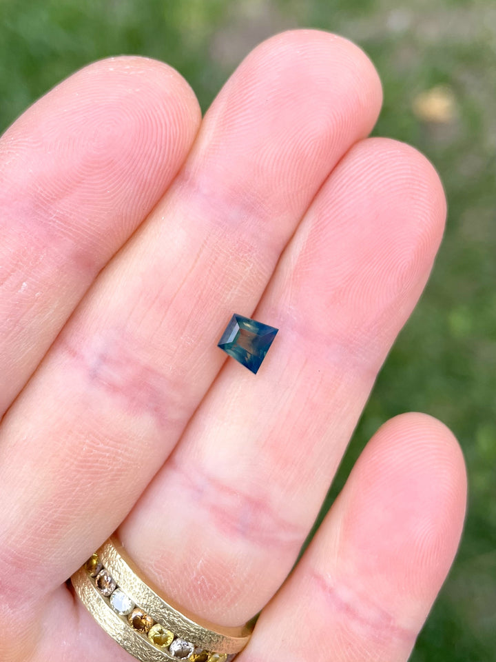 1.15 carat tapered baguette Australian sapphire with vivid green, yellow, and blue zoning held on fingertip