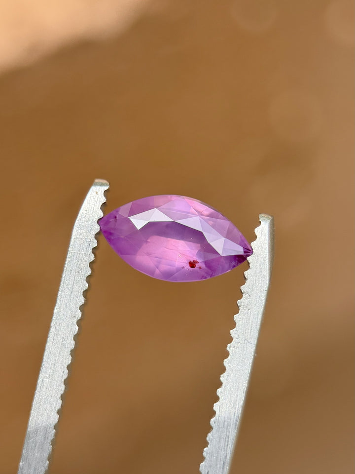 Close-up of 1.15 carat violet opalescent sapphire in marquise cut held in gem tweezers against a neutral background