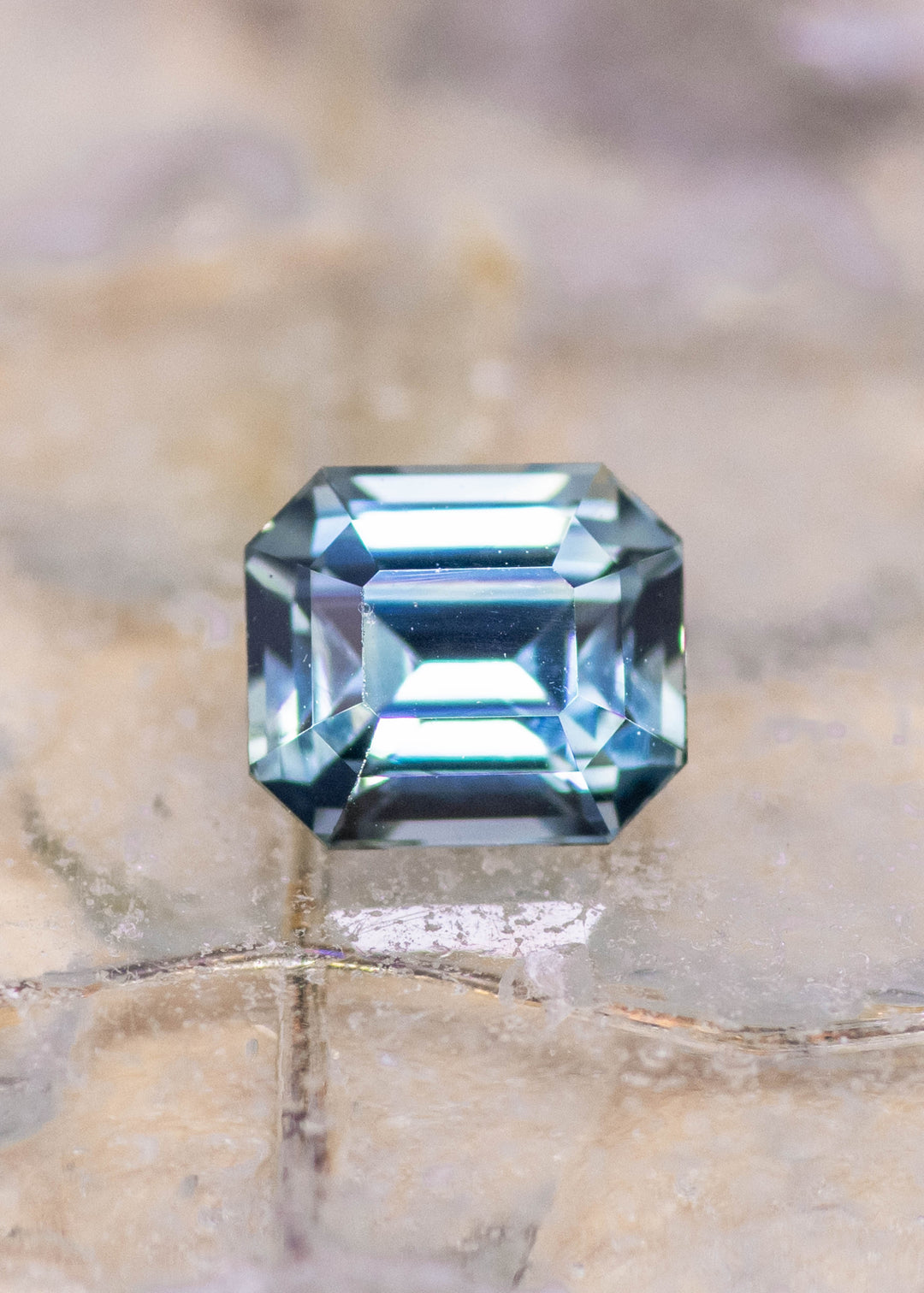 Loose blue and green sapphire from Sakaraha, Madagascar shown face-up on a display surface, highlighting the clean emerald step cut and natural teal tones