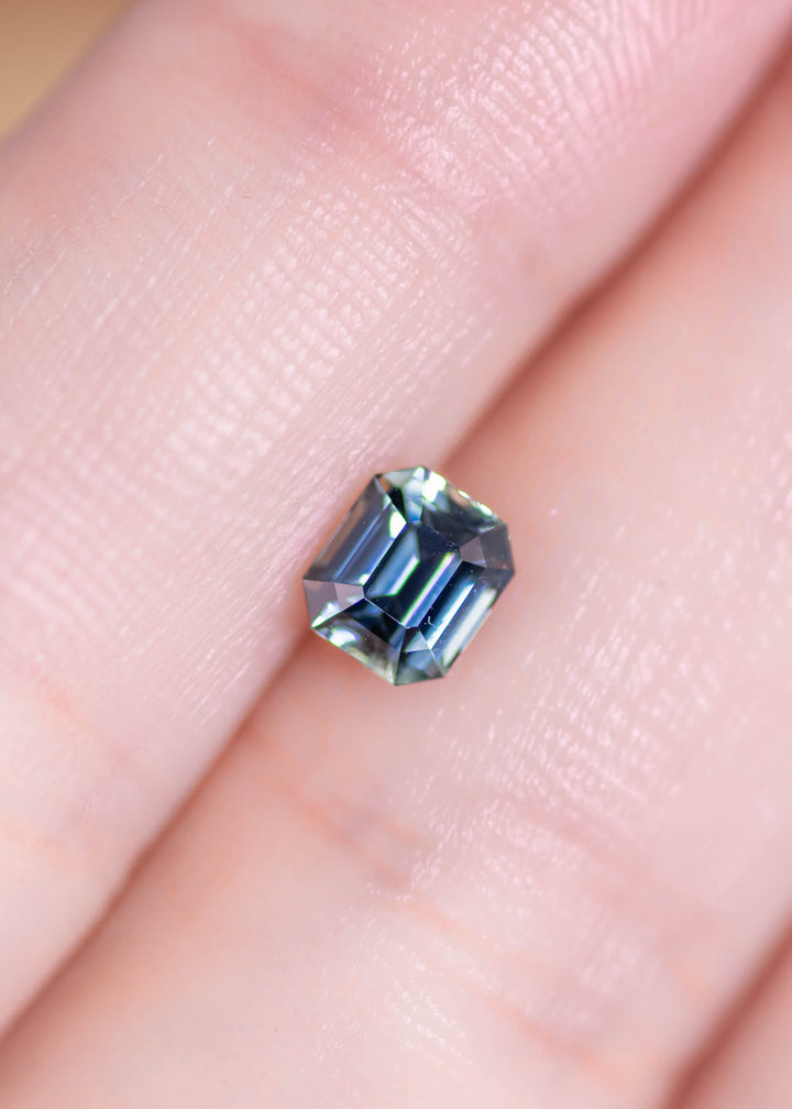 Loose emerald cut sapphire resting on fingertips, displaying blue and green tones and the structured step-cut pattern from Madagascar.