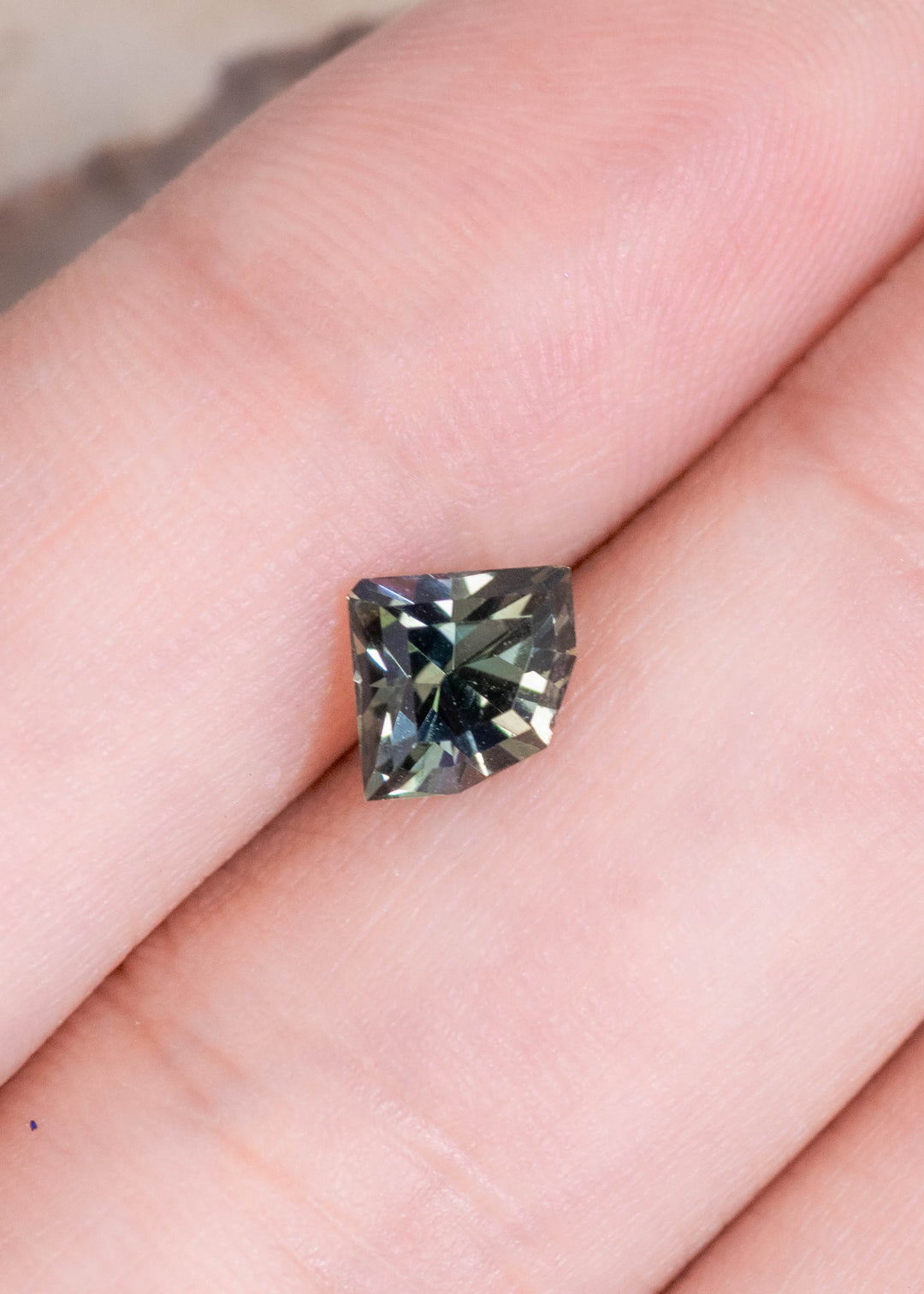 Loose green, teal, and yellow tanzanite resting on fingertips, highlighting the shield-shaped geometric mix cut and balanced proportions.