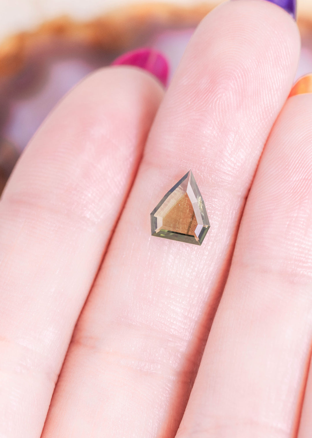 Loose olive green sapphire resting on fingertips, showing the geometric shield portrait cut and natural color from Gombe, Nigeria.