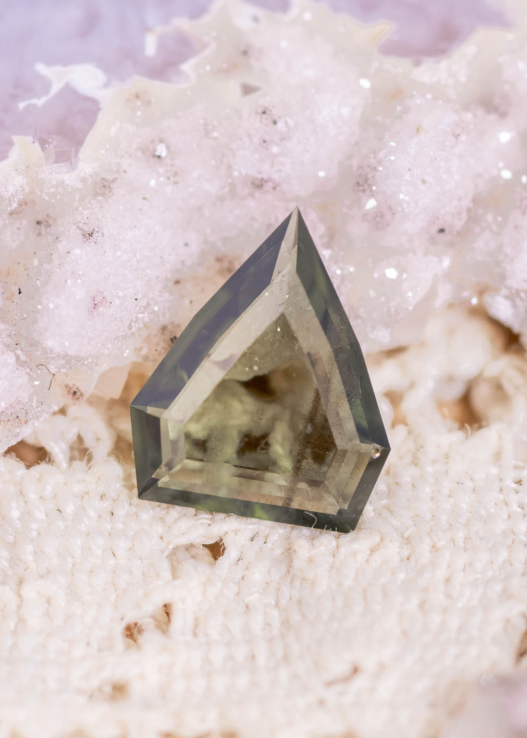 Loose olive green sapphire from Gombe, Nigeria shown face-up, highlighting the custom shield portrait cut and natural earthy green tone.
