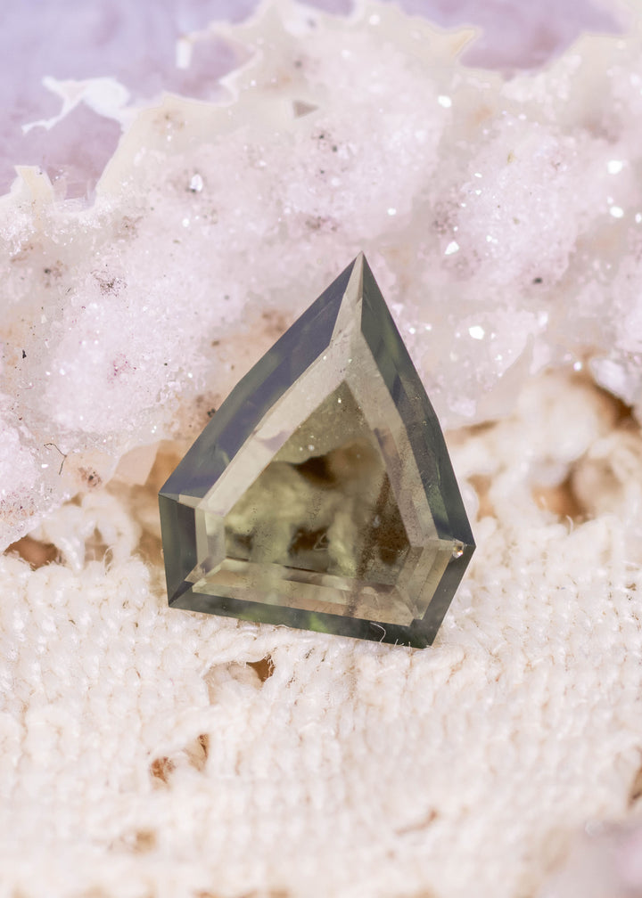 Loose olive green sapphire from Gombe, Nigeria shown face-up, highlighting the custom shield portrait cut and natural earthy green tone.