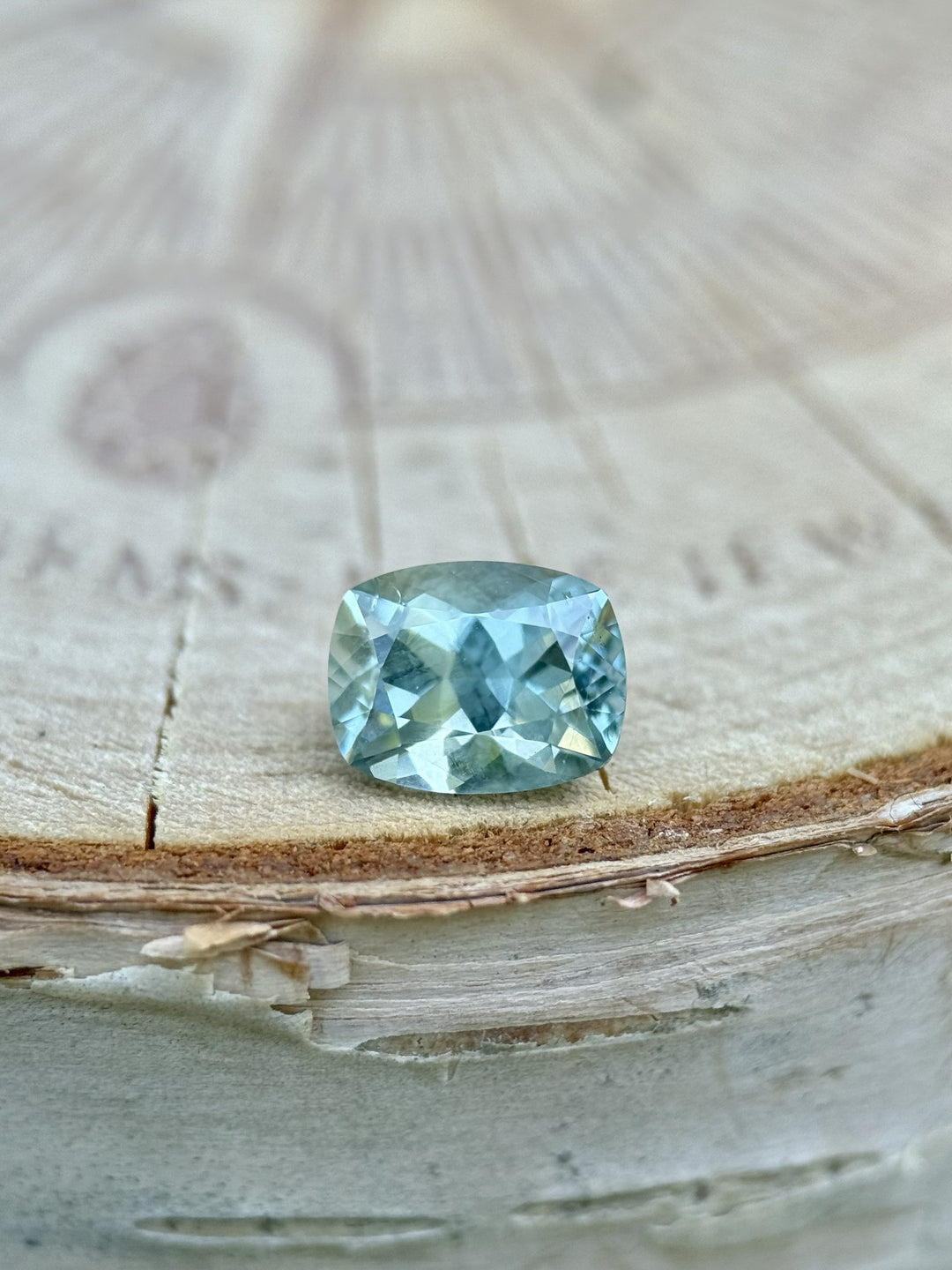 1.15 carat teal blue-green sapphire from El Dorado Bar, Montana resting on wood log, custom elongated cushion cut, untreated natural stone