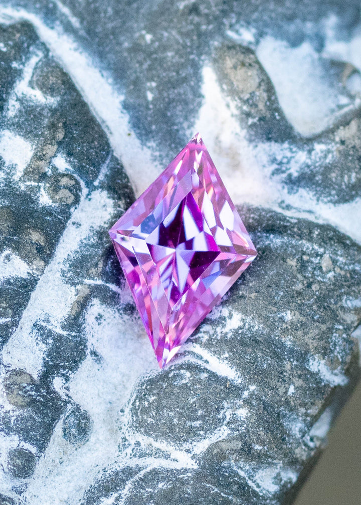 1.15ct hot pink custom kite rhombus cut sapphire resting on carved stone under natural light.