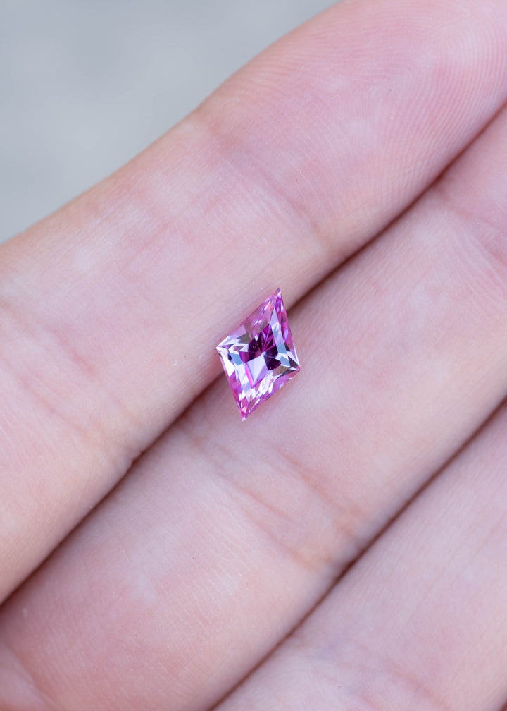 1.15ct hot pink custom kite rhombus cut sapphire held in finger tips to show color and scale.
