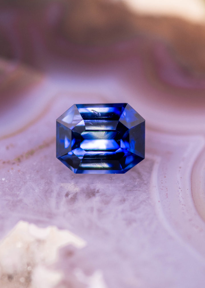 Loose blue bi-color sapphire from Ratnapura Sri Lanka shown face-up on stone displaying the clean emerald cut facets and natural blue to colorless color zoning.