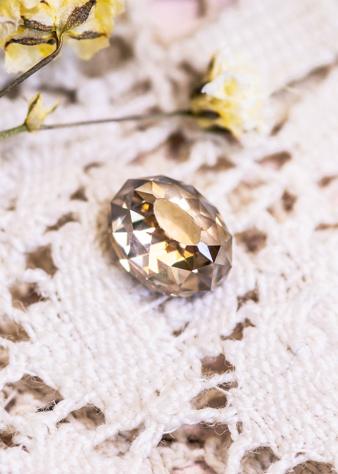 Loose fancy brown champagne diamond in Mughal cut displayed on a textured white surface with blurred yellow flowers in the background