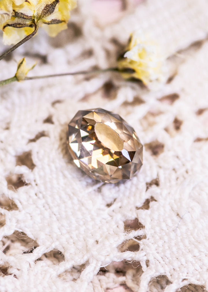 Loose fancy brown champagne diamond in Mughal cut displayed on a textured white surface with blurred yellow flowers in the background