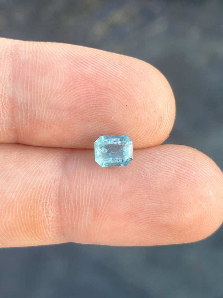 Close-up of a 1.17-carat green-blue emerald gemstone, emerald cut, displayed on a fingertip.
